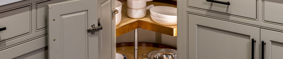Two-tier wood lazy susan in an open corner kitchen cabinet holding bowls and cookware